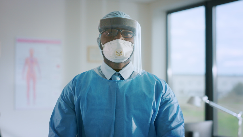 Portrait of an African American Doctor in Glasses is Wearing a Transparent Protective Face Shield, Mask and Overalls in a Hospital Room. Covid-19 Pandemic Concept About Slow Spread of Infectious Virus | Shutterstock HD Video #1059016382