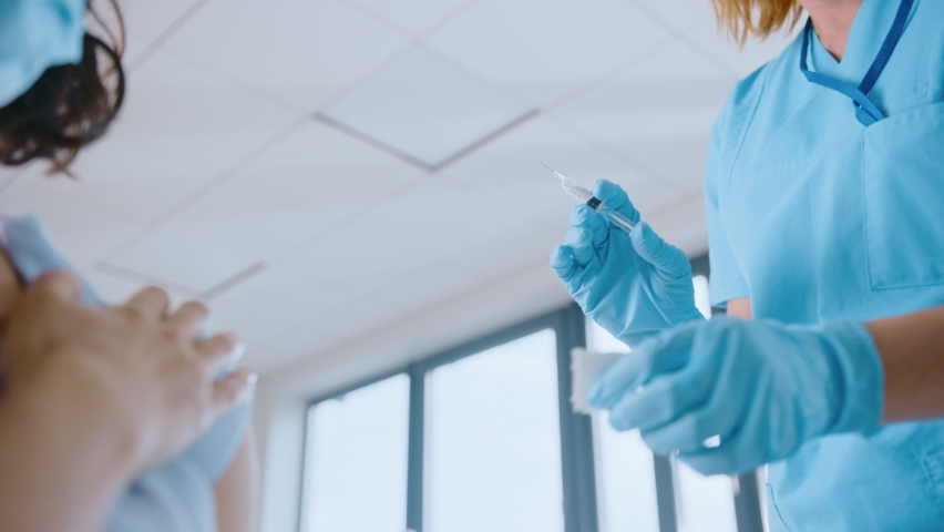 Medical Nurse in Safety Gloves and Protective Mask is Making a Vaccine Injection to a Female Patient in a Health Clinic. Doctor Uses Hypodermic Needle and a Syringe to Put a Shot of Drug as Treatment. | Shutterstock HD Video #1059016385