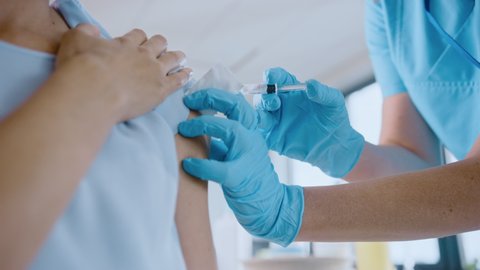 Medical Nurse in Safety Gloves and Protective Mask is Making a Vaccine Injection to a Female Patient in a Health Clinic. Doctor Uses Hypodermic Needle and a Syringe to Put a Shot of Drug as Treatment.