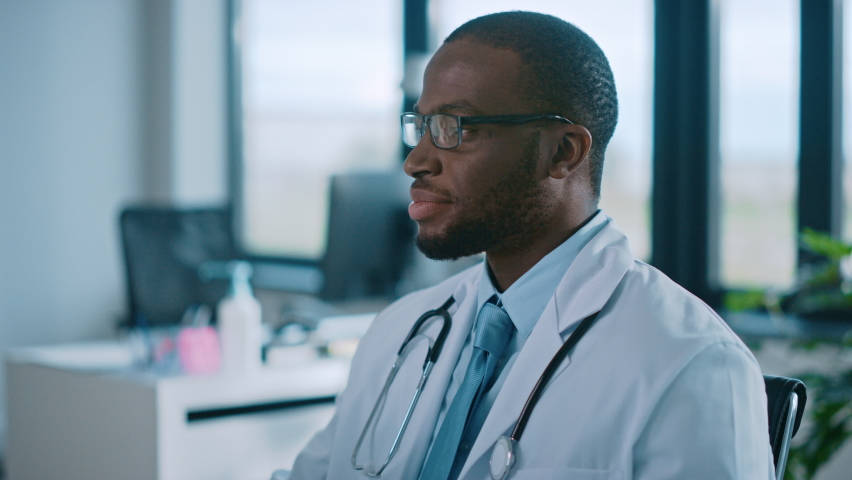 African American Family Medical Doctor in Glasses is Working in a Health Clinic. Successful Black Physician in White Lab Coat Looks at the Camera and Smiles in Hospital Office. | Shutterstock HD Video #1059016427