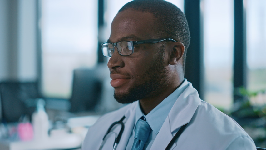 Close Up Portrait of African American Family Medical Doctor in Glasses is in Health Clinic. Successful Black Physician in White Lab Coat Looks at the Camera and Smiles in Hospital Office. | Shutterstock HD Video #1059016439