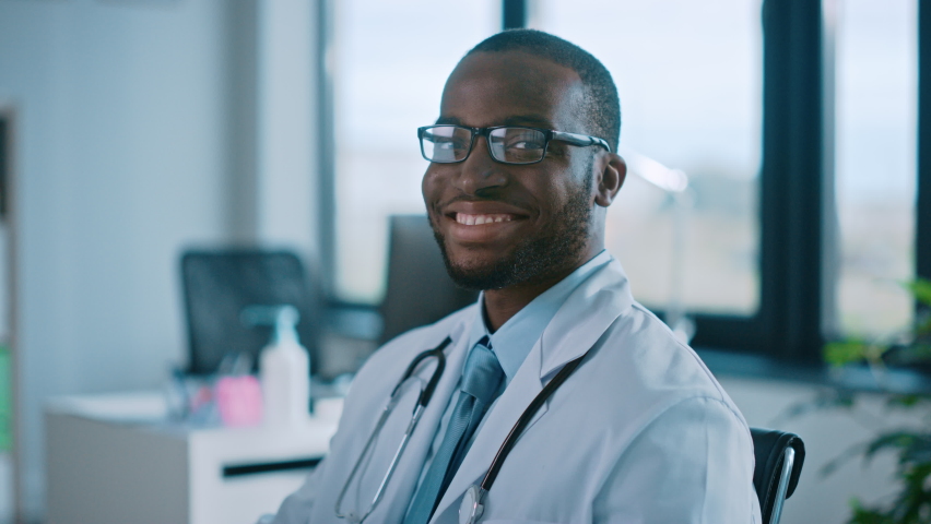 African American Family Medical Doctor in Glasses is Working in a Health Clinic. Successful Black Physician in White Lab Coat Looks at the Camera and Smiles in Hospital Office. | Shutterstock HD Video #1059016442
