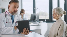 Friendly and Cheerful Family Doctor is Reading Medical History of Senior Female Patient During Consultation in a Health Clinic. Physician Using Tablet Computer in Hospital Office. - Powered by Shutterstock - Get 15% off with code: PIKWIZARD15