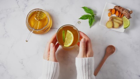 Female hands with white sweater holding a glass cup of anti-inflammatory turmeric ginger tea.