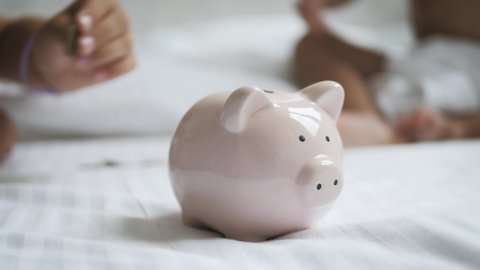Children save money in piggy bank in her home. Kid inserting a coin into a piggy bank, indoor financial concept. Kid saving money for future concept.