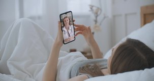 Female lie in bed at Home Using Smartphone to Talk to Her Doctor via Video Conference Medical App. Beautiful Woman Checks Possible Symptoms with Professional Physician, Using Online Video Chat.