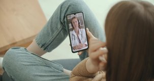 Female medical assistant wears white coat, headset video calling distant patient on smartphone. Doctor talking to client using virtual chat telephone app. Telemedicine, remote healthcare services 