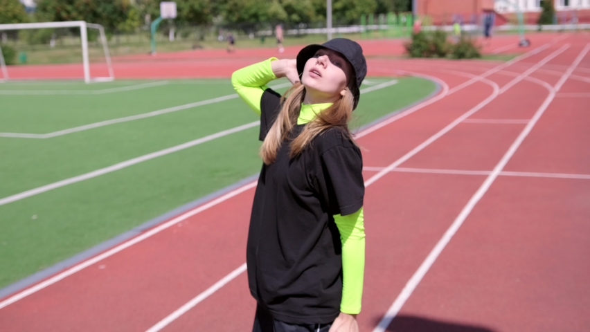 young girl dancer in a tracksuit and a hat dancing street dance, hip hop on a Sportsground. Performs spectacular elements of modern youth dance. Slow motion