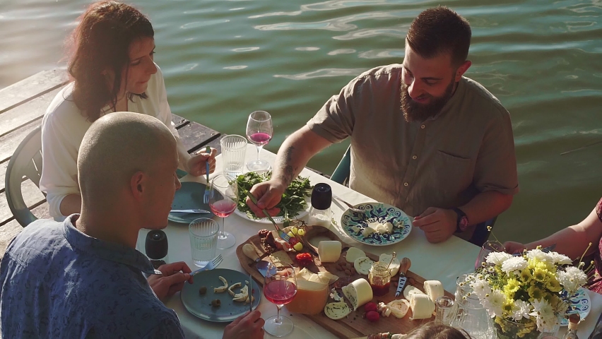 Slow motion shot of friends having dinner on jetty at lake