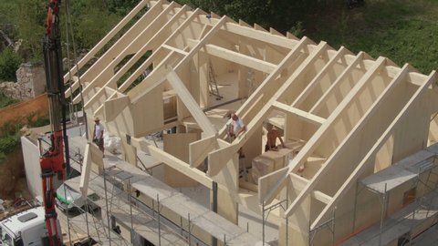 LJUBLJANA, SLOVENIA, MAY 2020,DRONE: Flying near a modern prefabricated house being built in the Slovenian countryside. Group of contractors mounts a wooden arch on the roof .