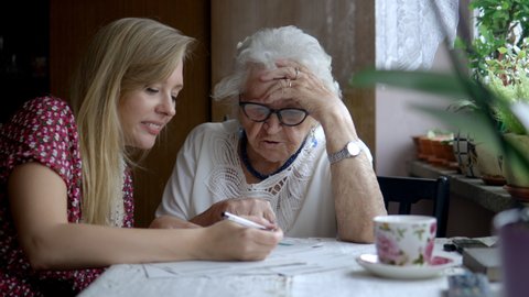 Young woman helping elderly grandmother with paperwork
