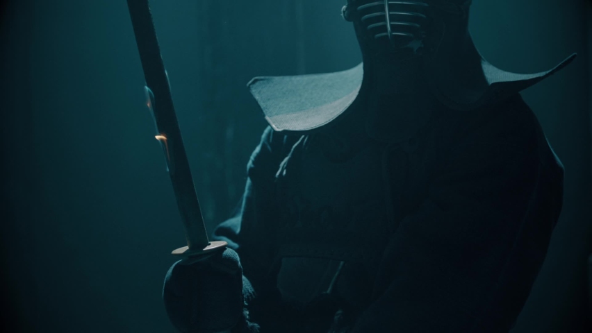 Portrait of a Japanese kendo fighter hold a burning sword . Epic Kendo warrior stands in armor in the fog and looking at the camera with his fire shinai . Mysterious video scene . Shot on Arri Alexa . Royalty-Free Stock Footage #1059036800