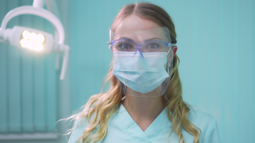 Young pretty woman dentist takes off her protective face mask and looks into the camera smiling. Close-up. | Shutterstock HD Video #1059037403