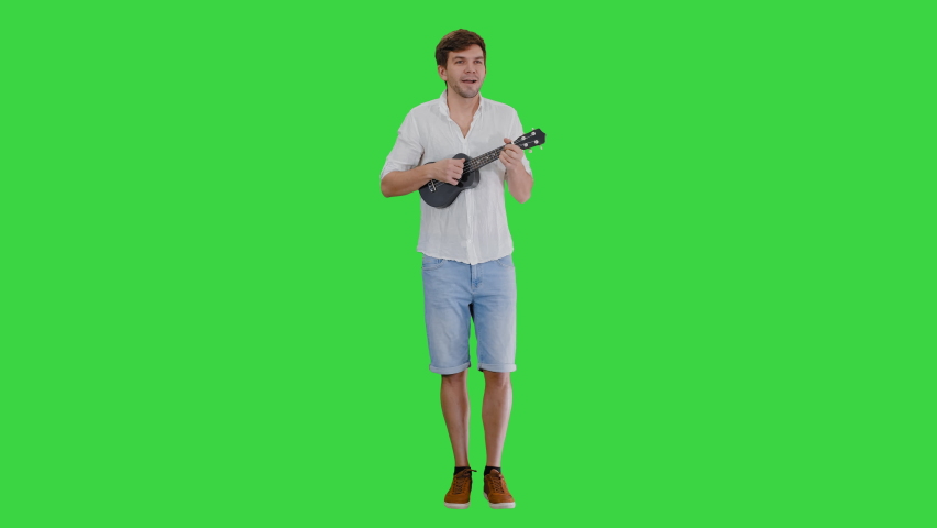 Smiling young man playing ukulele and singing looking into the camera on a Green Screen, Chroma Key.