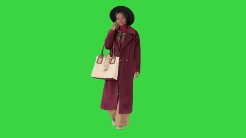 African american fashion woman in coat and black hat talking on the phone while walking on a Green Screen, Chroma Key.