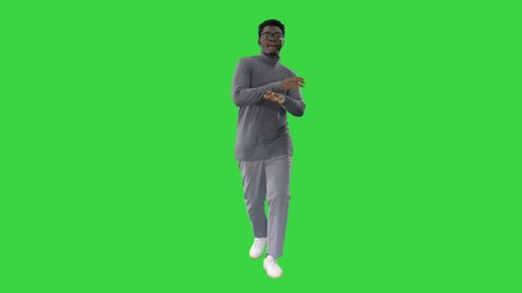 Young african american man in grey clothes and glasses grooving while walking on a Green Screen, Chroma Key.