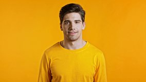 Portrait of handsome man in yellow t-shirt winking with eye, flirting and smiling to camera. Guy in studio on bright background.