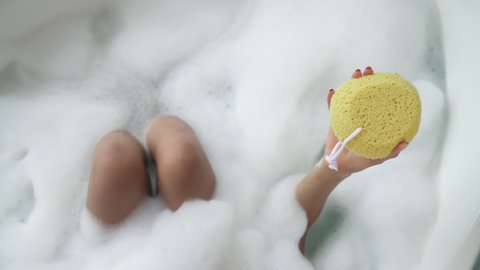 Top view of unrecognizable African woman taking bath with soap bubbles, holding shower sponge. Wellness concept.