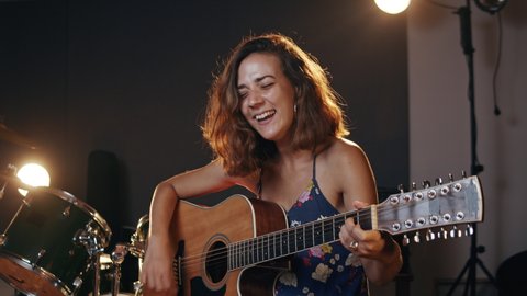 Music studio. Creative world. Musician. Latin woman playing guitar and singing in the recording studio. An attractive brunette female person in a beautiful shirt records songs. 