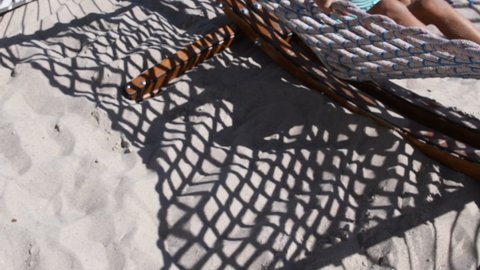 Defocus shadows of net hammock above clean beach sand. Silhouette of unrecognizable girl swinging in hammock. Leisure vacation concept