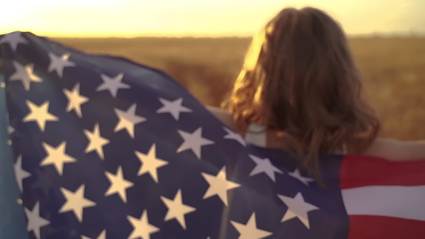 Girl in white dress wearing an American flag while running in a beautiful wheat field on sunset Royalty-Free Stock Footage #1059043514