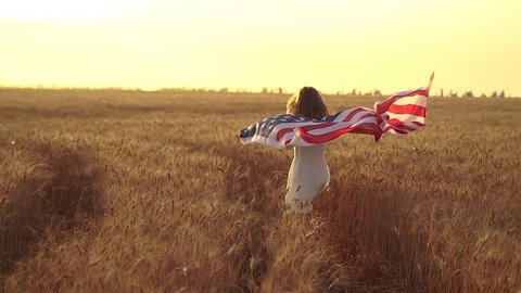 Girl in white dress wearing an American flag while running in a beautiful wheat field on sunset