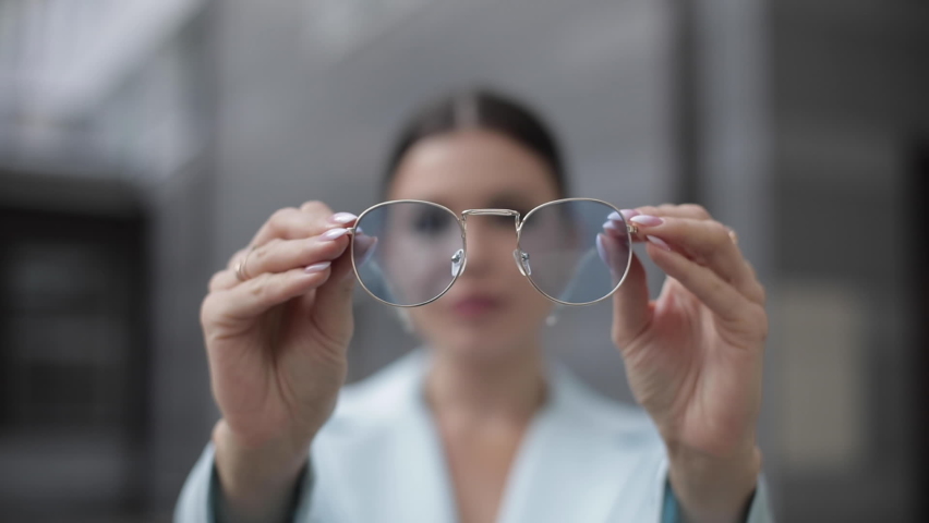 A young woman with a beautiful face and a slender figure holds her glasses and puts them on