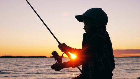 A child is using a fishing pole for fishing at sunset