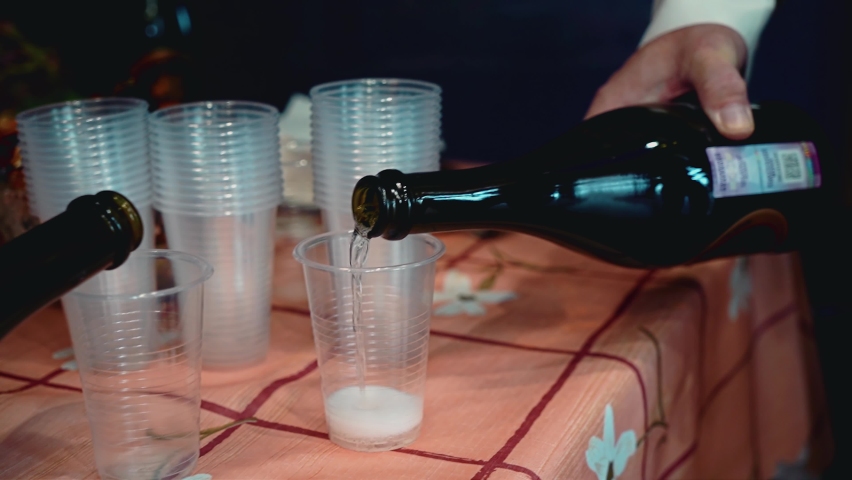 Two guys pouring champagne into plastic cups. Close-up of hands