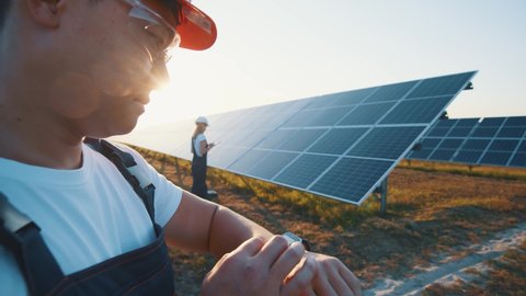 Futuristic asian engineer in helmet using smartwatch to control phorovoltaic power panels on ecological solar park. Virtual reality. Engineering. Holographic technology.