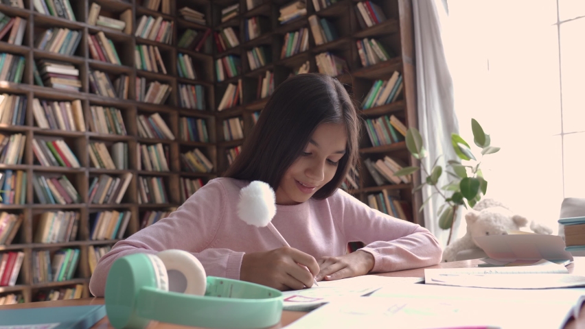 Cute smart indian latin preteen school girl pupil studying at home sitting at desk. Happy cute latin kid primary school student writing in exercise book doing homework, learning at table in classroom. Royalty-Free Stock Footage #1059048683