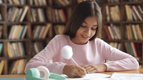 Smiling smart indian latin preteen school girl pupil studying at home sitting at desk. Happy cute hispanic kid primary school student writing in exercise book doing homework, learning at table. - Powered by Shutterstock - Get 15% off with code: PIKWIZARD15