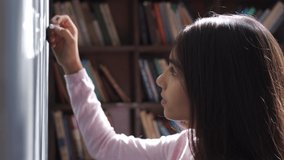 Serious indian kid primary school girl holding chalk writing on blackboard. Focused latin child preteen schoolgirl learning english alphabet letter handwriting standing in classroom. Close up view. - Powered by Shutterstock - Get 15% off with code: PIKWIZARD15