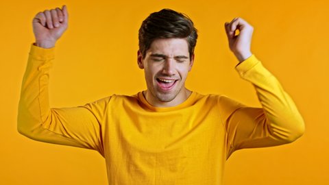 Happy european man dancing, showing yeah gesture of victory, he achieved result, goals. Surprised excited guy on yellow background