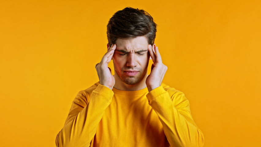 Young man having headache, studio portrait. Guy putting hands on head, isolated on yellow background. Concept of problems, medicine, illness | Shutterstock HD Video #1059048731