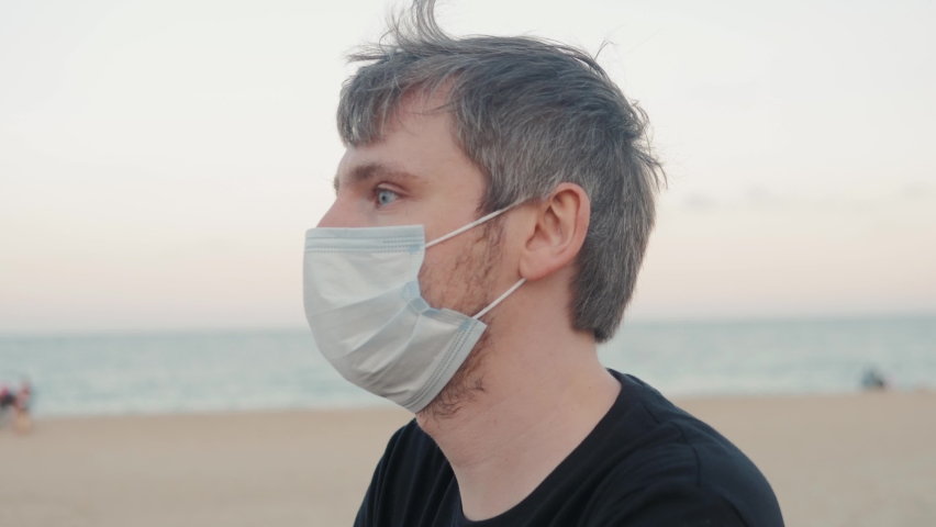 Man taking off mask after coronavirus quarantine is over, happy tourist drinking beer in bar on beach, the end of lockdown, first days after pandemic, happy student near sea.