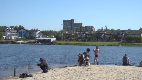 SEPTEMBER 13, 2020 - ZAPORIZHYA, UKRAINE: fishermen in the morning in the city on the sandy shore catch fish on fishing rods, on the back of the house trees and sky