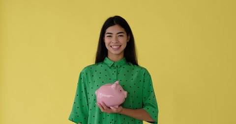 Smiling woman inserting coin into piggy bank