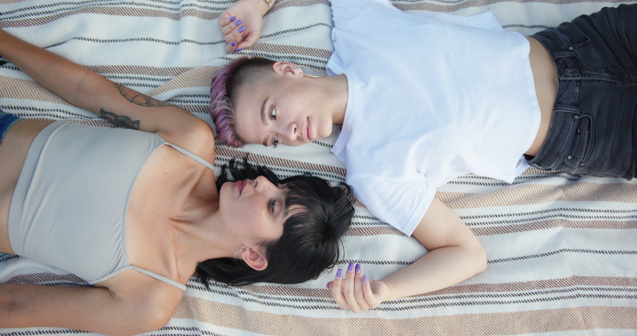 Happy loving lesbian LGBT couple lie on the bedspread in the park and looking at each other