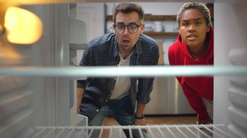 Multiethnic young couple looking into an empty refrigerator in kitchen. View from inside of hungry diverse man and woman opening fridge finding nothing to eat