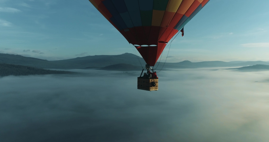 Colorful hot air balloon epic flying above mountain over the fog at sunrise with beautiful sky background - High altitude aerial drone wide view | Shutterstock HD Video #1059059570