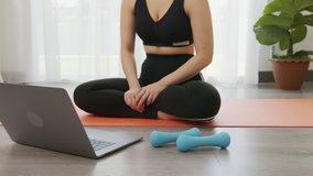 Asian women doing yoga exercises with blue dumbbells by themselves and watch video tutorials online from the laptop in the living room at home.