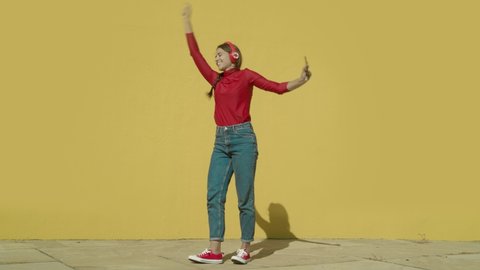 Young Happy Latin Woman wearing red shirt and jeans and red converse shoes starts dancing with a yellow background wall on a sunny day wide-angle shot