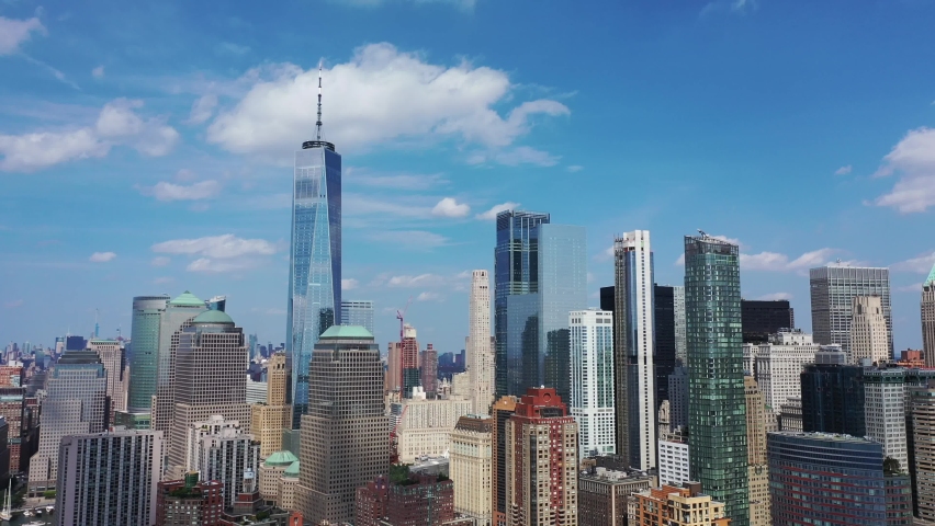 An aerial view over lower Manhattan. The drone trucks and pans right, orbiting the buildings. The freedom tower is the main attraction on this beautiful day with blue skies and a few clouds. Royalty-Free Stock Footage #1059068228