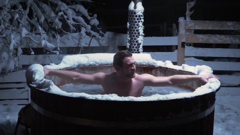 Man taking a freezing cold, ice bath in a outdoor pool. on a dark, winter evening- Static, slow motion shot