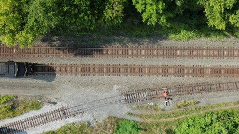 Black diesel locomotive train engine with headlight on, stopped on railroad track, top down overhead aerial drone perspective, switching car, track, freight and travel transportation concept