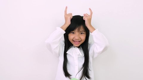 Young Asian child girl is wearing braces and is smiling cute and takes her fingers to act like cow horns on white background