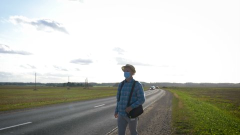A young man is hitchhiking around the country. The man is trying to catch a passing car for traveling. The man with the backpack went hitchhiking to south.