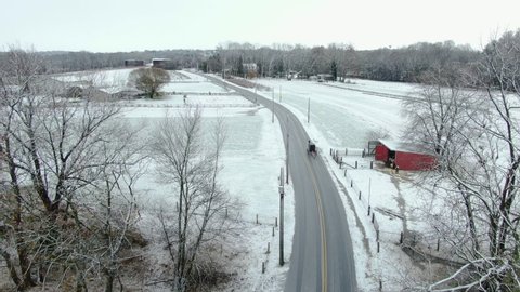 Pennsylvania countryside covered in thin layer of first seasonal snow, a horse carriage on empty road passing by wooden shed in bright red color