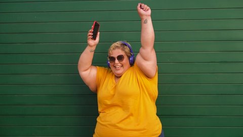 Happy plus-size woman dancing and listening music with smartphone - Party concept - Slow Motion